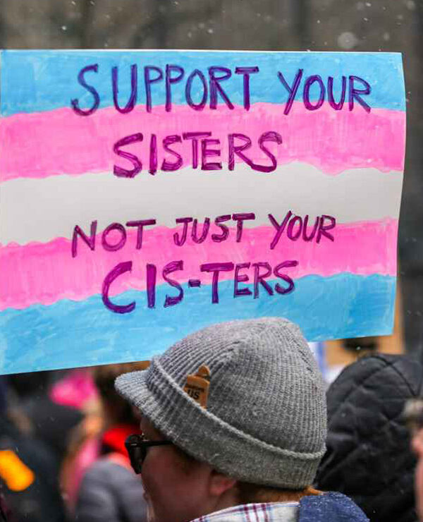 A demonstration sign reading "Support Your Sisters, Not Just Your Cis-ters."