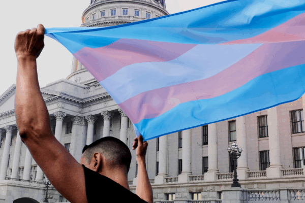 A person holding a transgender pride flag in front the Utah State Capitol.