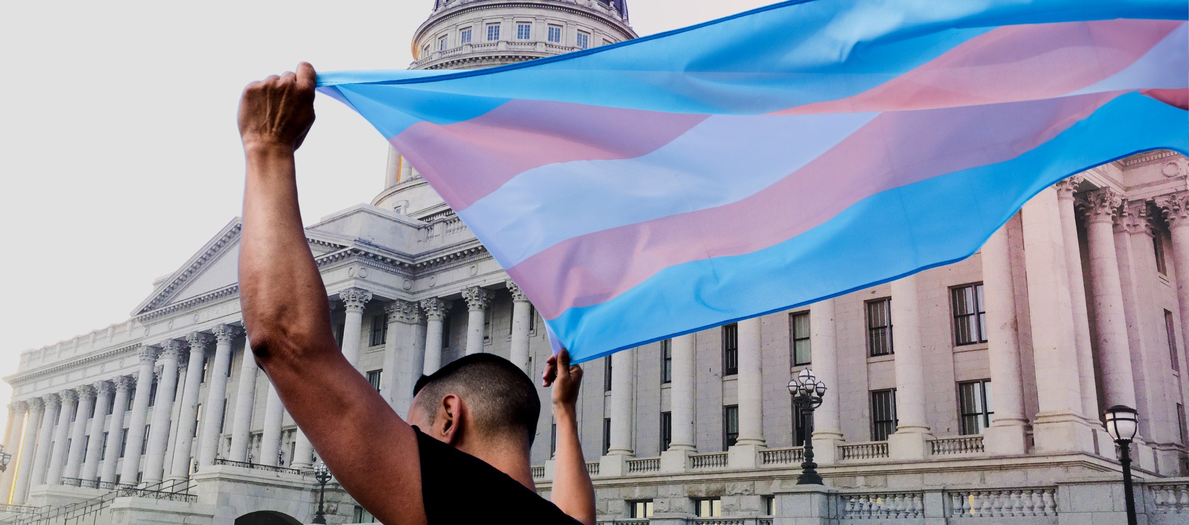 A person holding a transgender pride flag in front the Utah State Capitol.