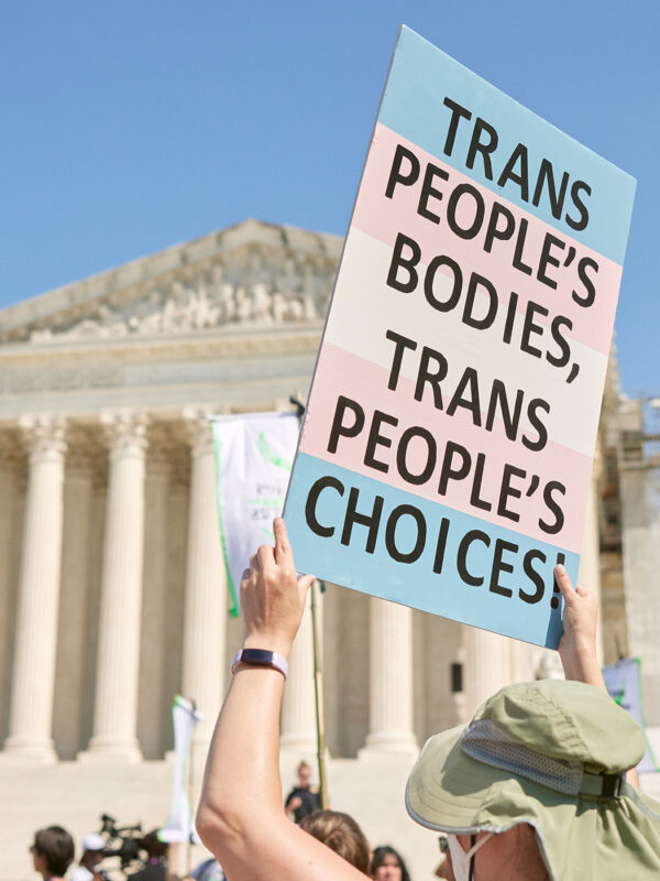 A demonstrator at a march in front of the Supreme Court holds up a sign reading "TRANS PEOPLE'S BODIES, TRANS PEOPLE'S CHOICES".