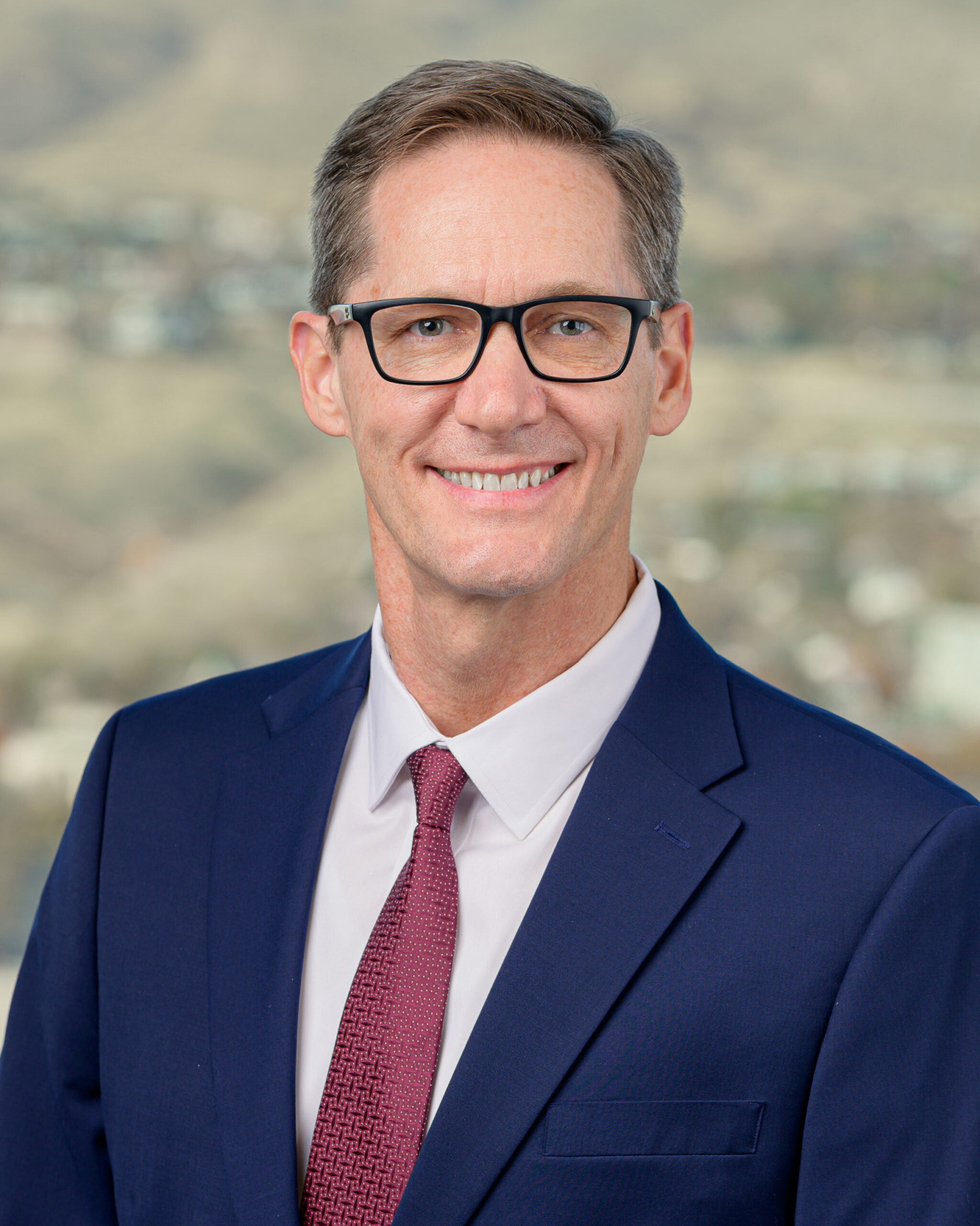 A headshot of David W. Tufts. he is wearing a blue suit with white undershirt and a red tie.