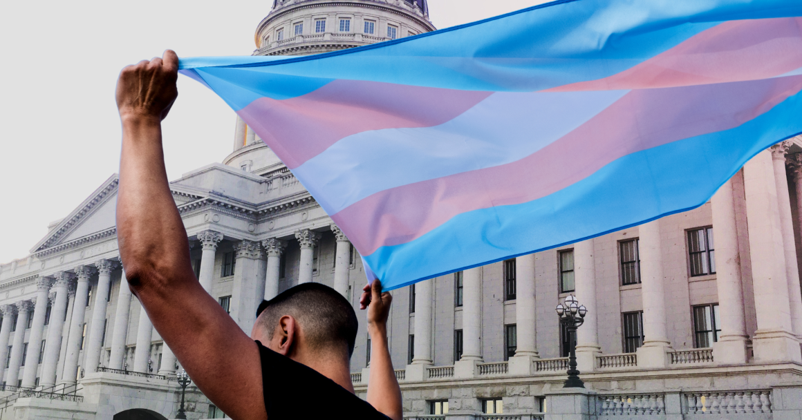 A person holding a transgender pride flag in front the Utah State Capitol. 