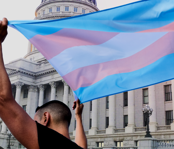 A person holding a transgender pride flag in front the Utah State Capitol. 